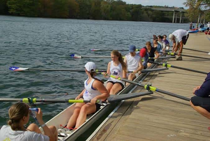 Equipo de remo en el muelle del Texas Rowing Center, con remos y chalecos visibles, durante una sesión de entrenamiento
