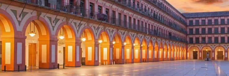 Fachada iluminada de la Plaza de la Corredera al atardecer con arcos y balcones