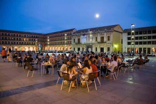 Plaza de la Corredera durante la noche con mesas y gente disfrutando del ambiente