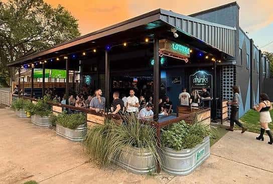 Vista exterior del Little Drinks Lounge con terraza al atardecer y ambiente festivo