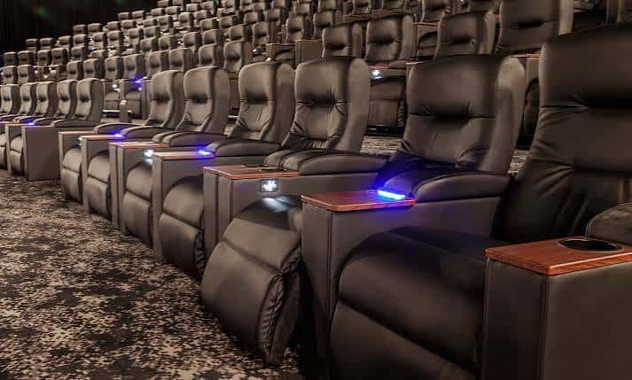 Interior del cine con butacas de cuero reclinables y mesitas laterales