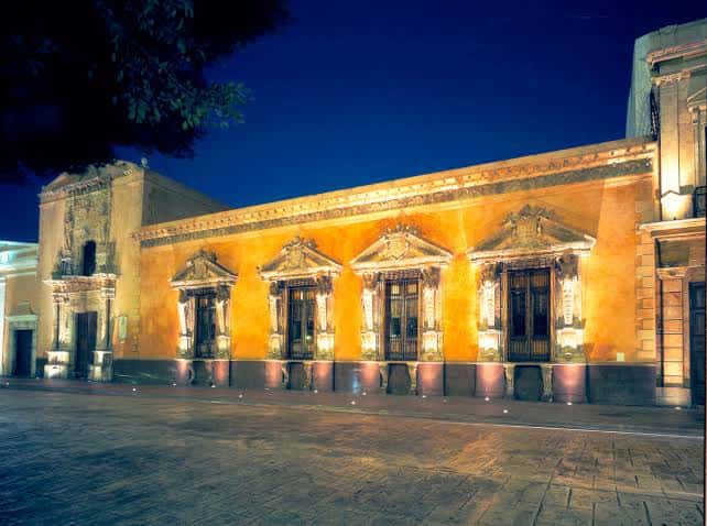 Vista nocturna de la fachada iluminada del Museo Casa Montejo con cielo azul oscuro y pavimento de piedra