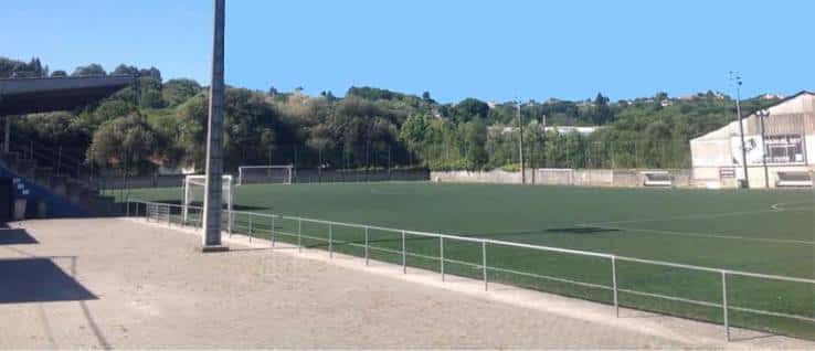 Vista panorámica del campo de fútbol con céspede artificial y gradas bajo cielo despejado