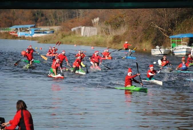 Competición de piragüismo en la ría con participantes en trajes rojos y gorros de Papá Noel