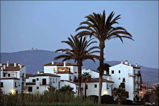Vista nocturna de la urbanización Pueblo del Chirimoyo con palmeras y montañas al fondo