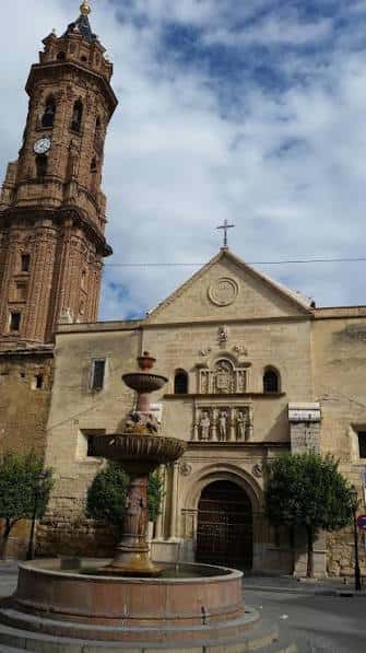 Fachada frontal de la iglesia con fuente en primer plano bajo cielo parcialmente nublado