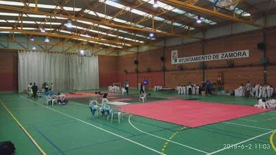 Interior del polideportivo configurado para evento deportivo con tatamis rojos y espectadores sentados