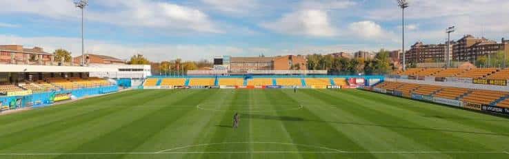 Panorámica del campo de fútbol con gradas vacías bajo cielo despejado