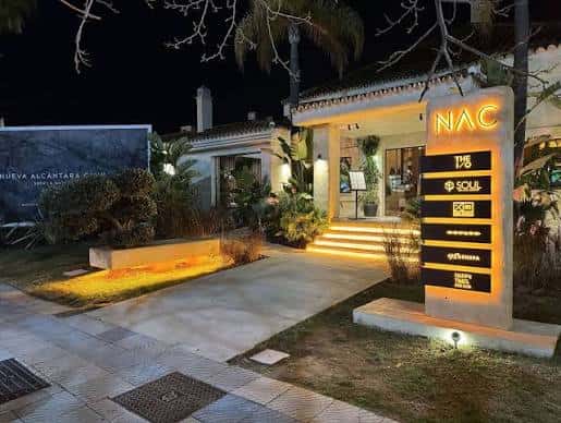 Entrada nocturna del club con iluminación cálida y señalización luminosa 'NAC'