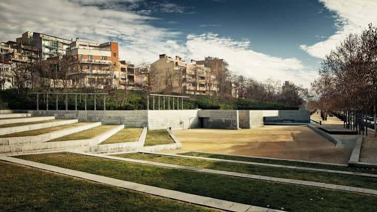 Plaza central del parque con zonas de césped y bancos de hormigón bajo un cielo despejado