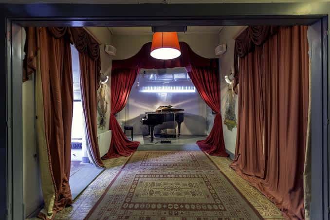 Vista interior del auditorio con cortinas rojas, piano de cola y alfombra decorativa