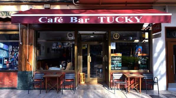 Fachada del Café Bar Tucky con toldo rojo y mesas exteriores