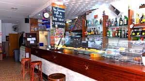 Interior del bar mostrando la barra de madera y estanterías con botellas