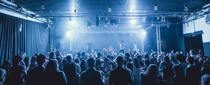Sala de conciertos con banda actuando bajo luces blancas y ambiente festivo