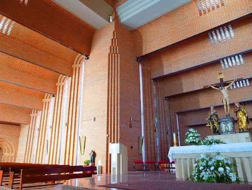 Interior de la iglesia mostrando el altar principal, crucifijo y bancos de madera en ambiente luminoso