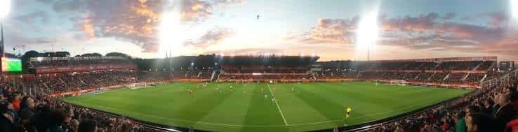 Estadio Montilivi durante un partido con espectadores y luces encendidas al atardecer