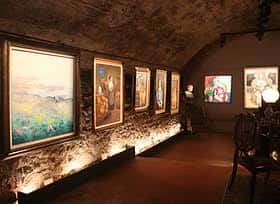 Interior de la galería con obras expuestas en paredes de piedra
