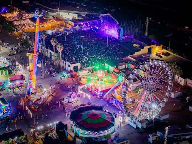 Vista aérea nocturna del recinto ferial con atracciones y escenario