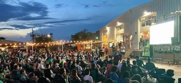 Vista exterior de Hopsquad Brewing Co. durante un evento al aire libre con una gran pantalla y público reunido