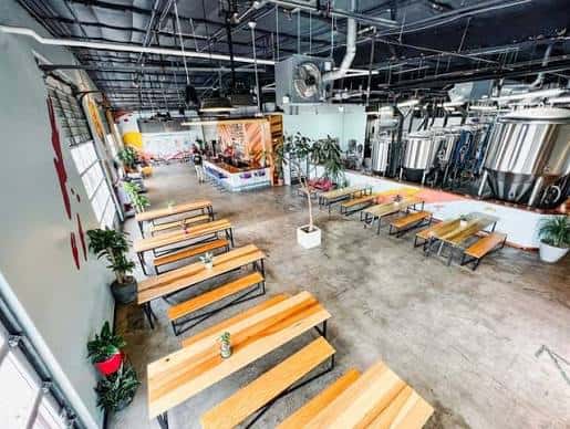 Interior espacioso de la cervecería con tanques de fermentación, mesas de madera y decoración industrial