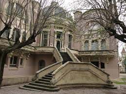 Fachada principal del edificio histórico con detalles arquitectónicos y jardines circundantes