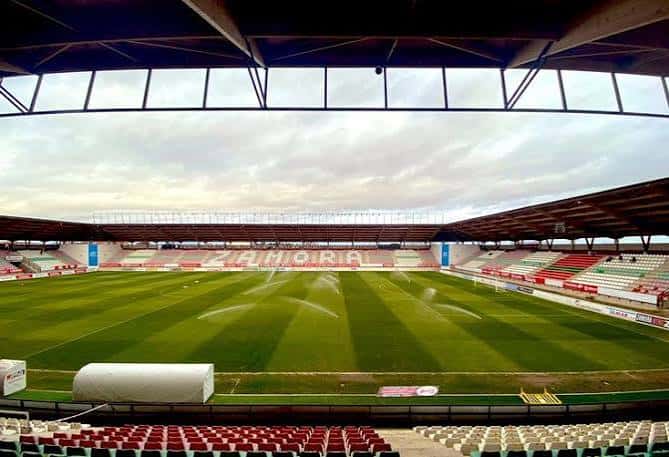 Panorámica del estadio mostrando las tribunas con el nombre 'ZAMORA' en los asientos y riego activo