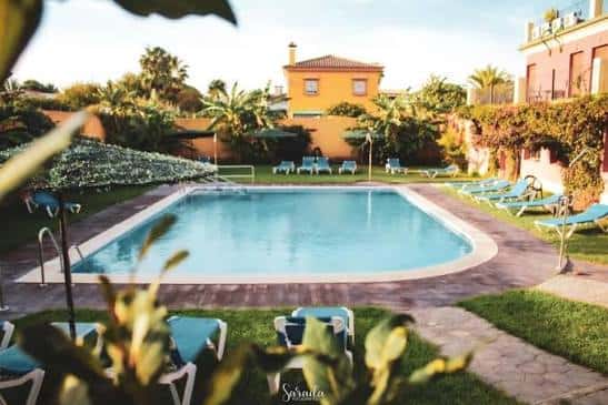Piscina exterior rodeada de tumbonas y jardines tropicales al atardecer