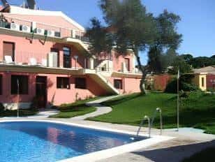 Fachada rosa del hotel junto a la piscina bajo cielo despejado
