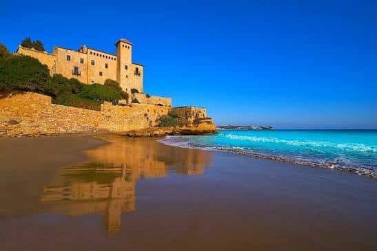 Reflejo del Castillo de Tamarit en la arena mojada de Cala Jovera bajo cielo azul intenso