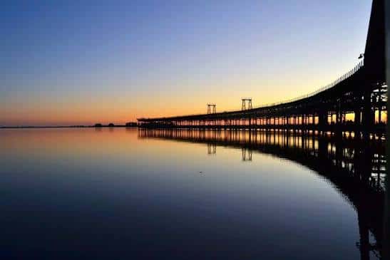 Silueta del muelle al atardecer reflejada en el agua tranquila