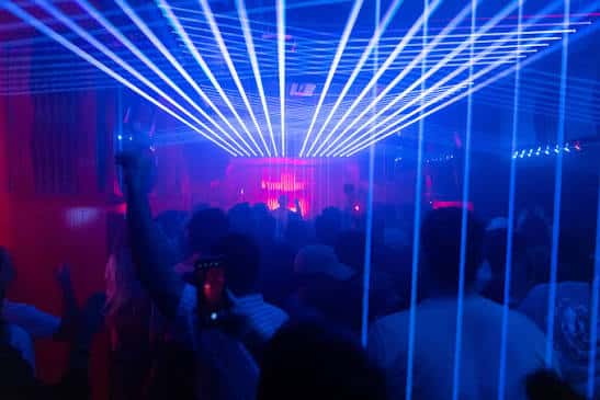 Interior del club Les Enfants Brillants con luces láser azules y gente bailando