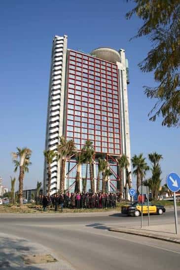 Vista exterior del Hyatt Regency Barcelona Tower con palmeras y grupo de personas en la entrada