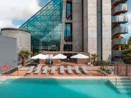 Piscina exterior del hotel con tumbonas y sombrillas bajo el edificio moderno