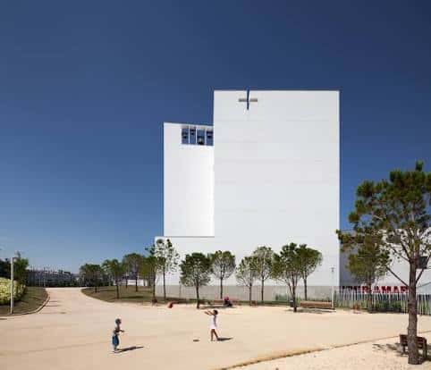 Fachada frontal de la iglesia bajo un cielo azul despejado con niños jugando en el patio