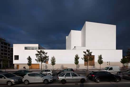 Exterior de la parroquia con arquitectura moderna blanca y estacionamiento frente a ella