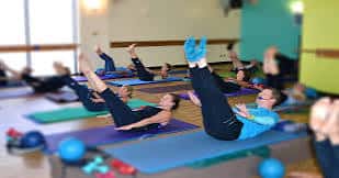 Clase de Pilates en grupo sobre esterillas azules con equipamiento deportivo al fondo