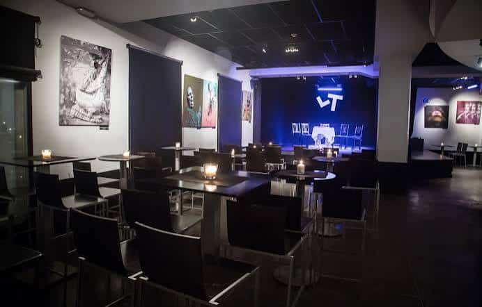Interior del tablao con mesas, sillas y escenario iluminado en azul