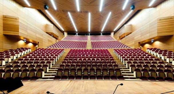 Interior del auditorio principal con butacas rojas y techo acústico de madera