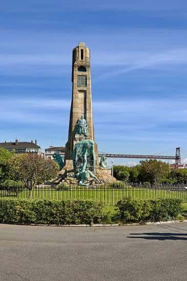 Monumento central del muelle con esculturas y el puente Vizcaya en el horizonte