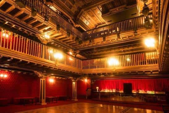 Interior del Teatro Magno con butacas rojas y balcones de madera