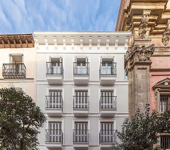 Detalle de la fachada blanca con balcones ornamentados junto a estructura histórica
