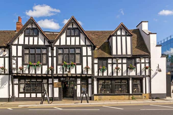 Fachada principal del Black Swan Inn con estilo Tudor y macetas colgantes