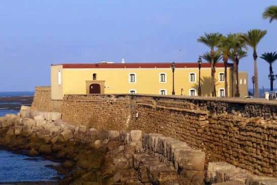Fachada exterior amarilla del edificio junto a la muralla y palmeras