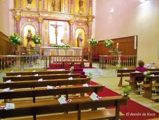 Interior del altar mayor con retablo dorado, crucifijo central y bancos de madera