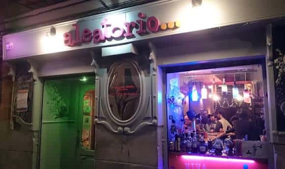 Vista nocturna de la fachada del Aleatorio Bar con su letrero iluminado y ambiente interior visible