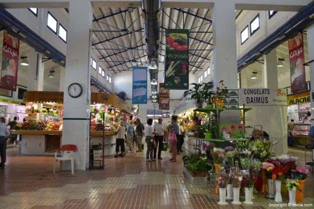 Vista interior del mercado mostrando puestos de flores y productos frescos bajo techo metálico