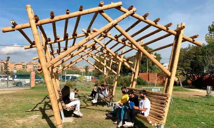 Área de descanso al aire libre con estructura de bambú y estudiantes sentados en el patio