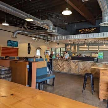 Interior del bar principal con mostrador de madera en zigzag, iluminación industrial y personal atendiendo