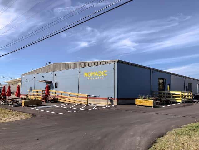 Vista exterior del edificio de Nomadic Beerworks con su logotipo amarillo y zona de terraza al aire libre
