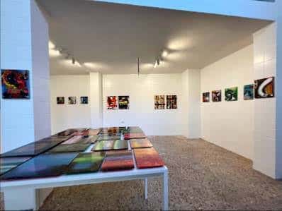 Interior de la Galería Modesta mostrando una exposición de arte abstracto con obras en mesas y paredes